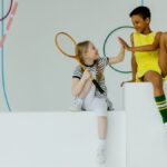 Two children having fun indoors with tennis gear. High-five moment.