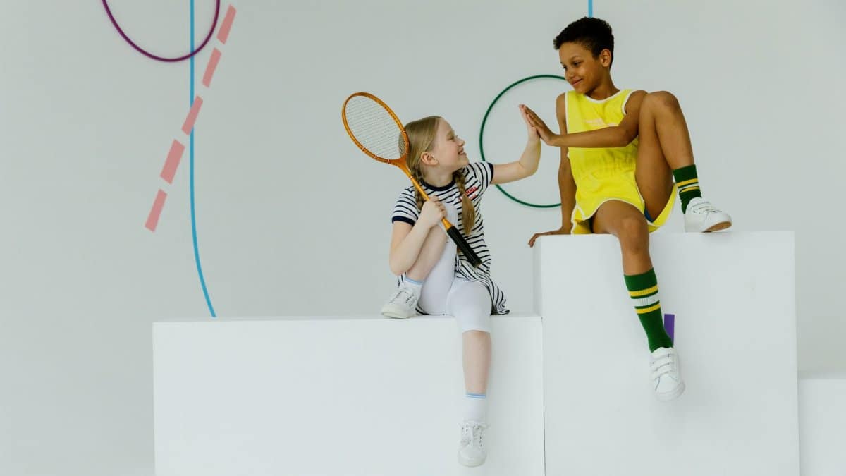 Two children having fun indoors with tennis gear. High-five moment.