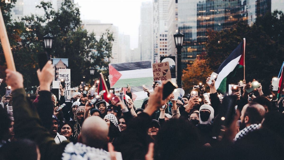 Large group of protesters in an urban setting holding Palestinian flags, expressing unity and peace.