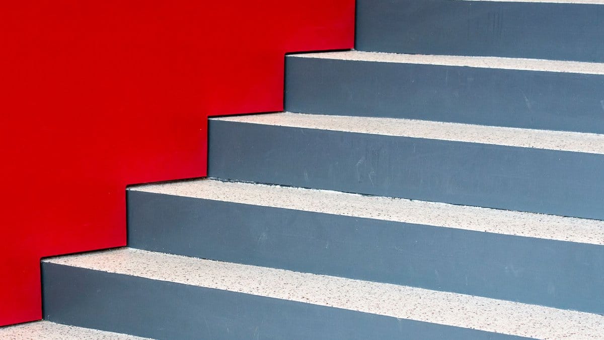 Image of a modern staircase against a vibrant red wall, highlighting geometric design and contrast.
