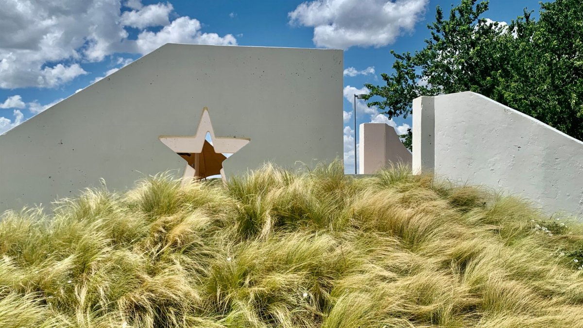 White wall with star cutout amidst grassy field under a vibrant blue sky in Texas.