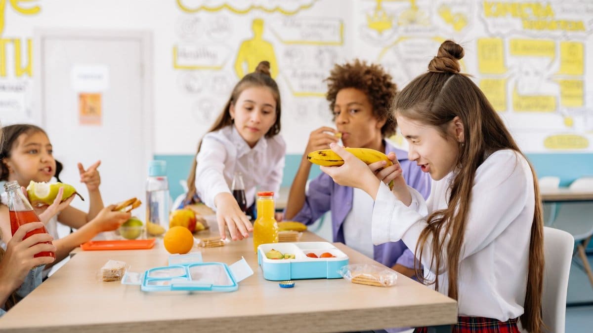 Group of students sharing healthy snacks and drinks in a vibrant school cafeteria setting.