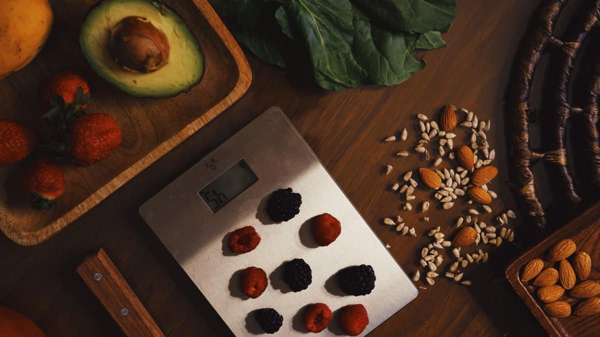 Top view of composed raw almond with seeds and avocado on table with berries on scales for cooking healthy dish