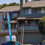 House being renovated with workers on a hydraulic lift in an urban area.
