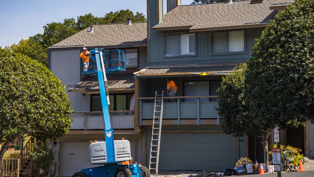 House being renovated with workers on a hydraulic lift in an urban area.