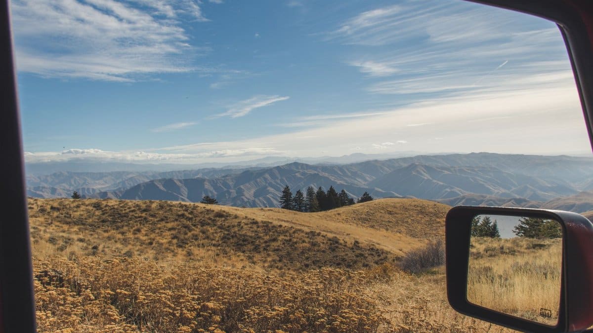 Breathtaking view of mountains and fields through a car window during a sunny autumn day.