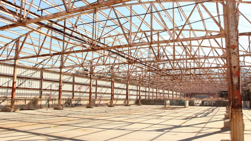 Rusty metal framework of an empty warehouse under clear blue sky.