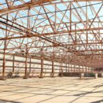 Rusty metal framework of an empty warehouse under clear blue sky.