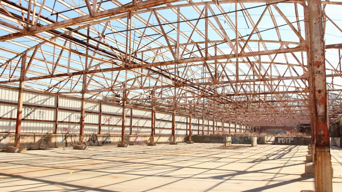 Rusty metal framework of an empty warehouse under clear blue sky.