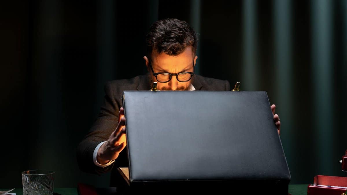 A man in a black suit is intriguingly opening a briefcase in a dimly lit room.