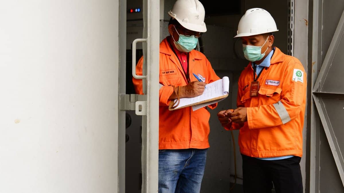 Two construction workers in safety gear discussing plans at a site entrance.