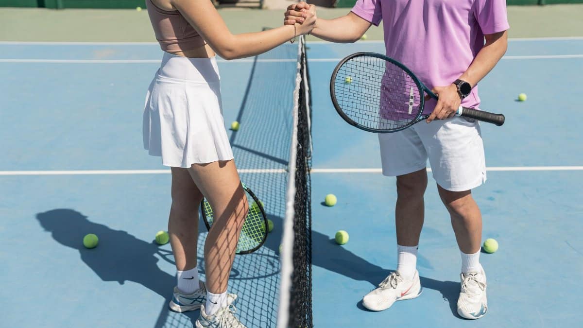 Two tennis players shaking hands over the net on a sunny day, symbolizing sportsmanship.