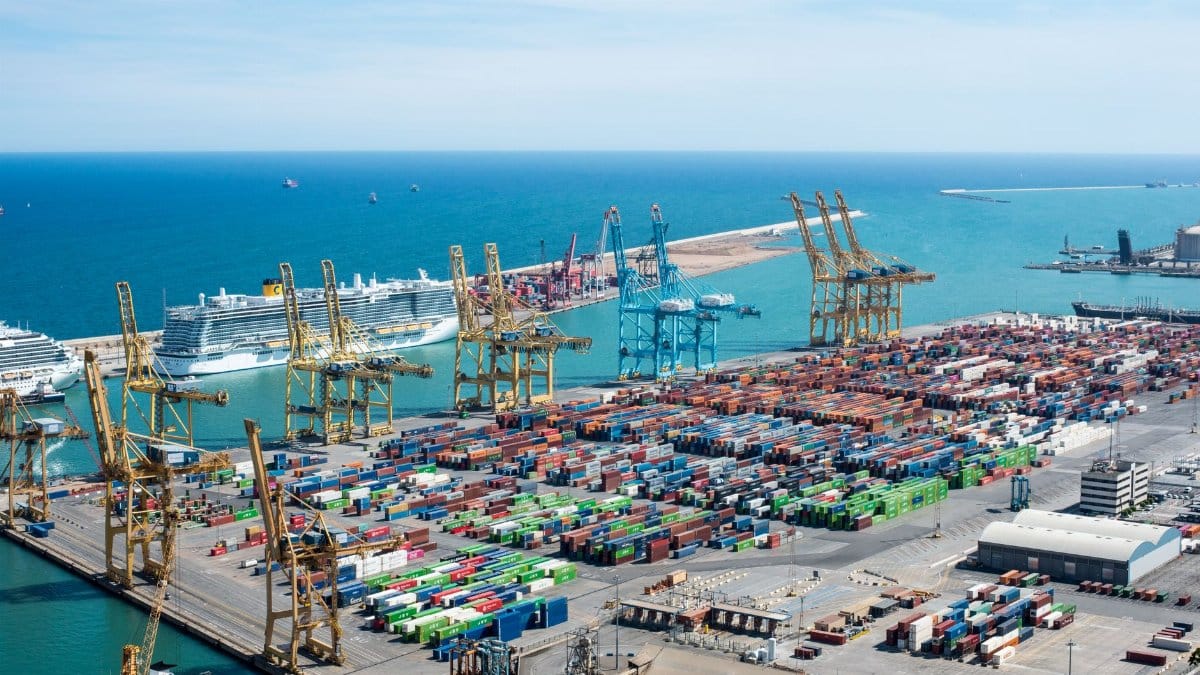 A vibrant aerial shot of Barcelona port featuring cranes, containers, and cruise ships on a sunny day.