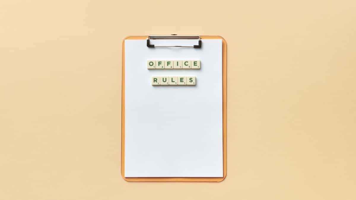 A clipboard with the phrase 'Office Rules' spelled out using Scrabble tiles on a beige background.