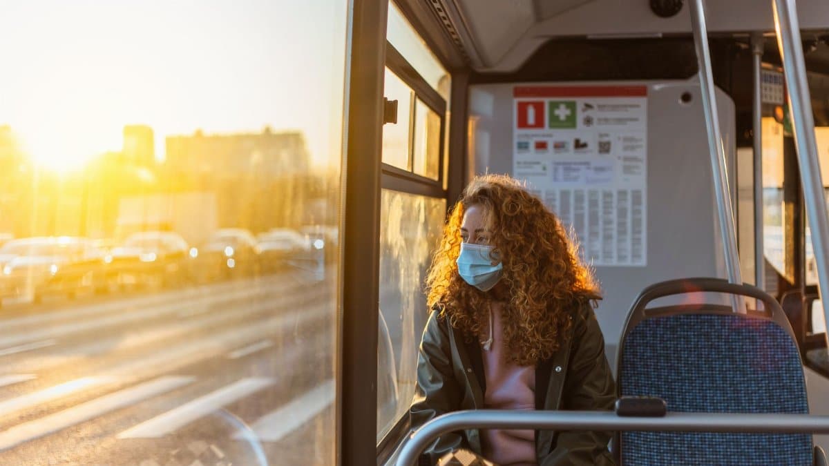 Woman wearing a mask on a bus during sunset, reflecting the pandemic era lifestyle.