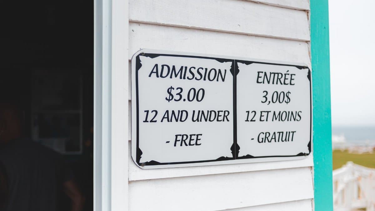 Bilingual sign displaying admission prices in English and French at building entrance.
