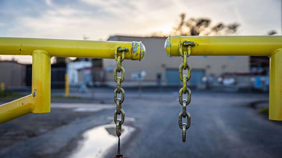 A yellow barrier with chains blocks an industrial road at dusk, symbolizing security and restriction.