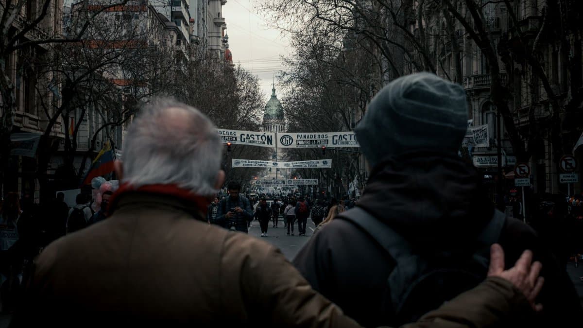 Crowds gather at a street demonstration in Buenos Aires, Argentina, with historic architecture in the background.