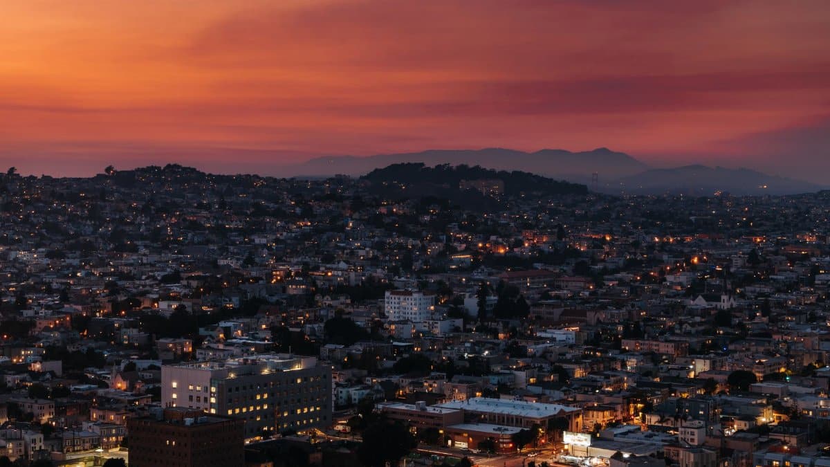 Aerial view of city with residential buildings against hills under colorful sky at sunrise