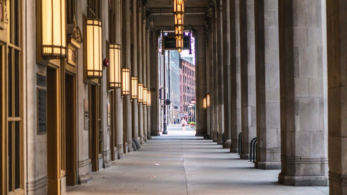 A view down an elegant corridor lined with tall columns and warm glowing lights. Urban setting.