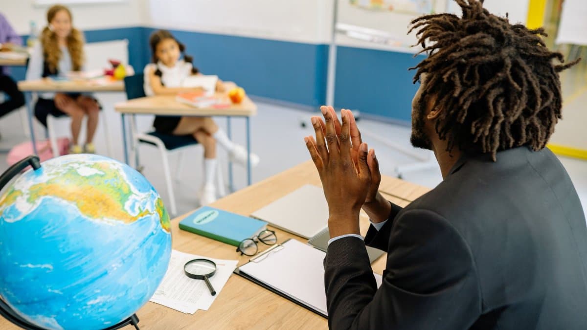 A teacher in a classroom with students, focusing on a globe for geography lesson.