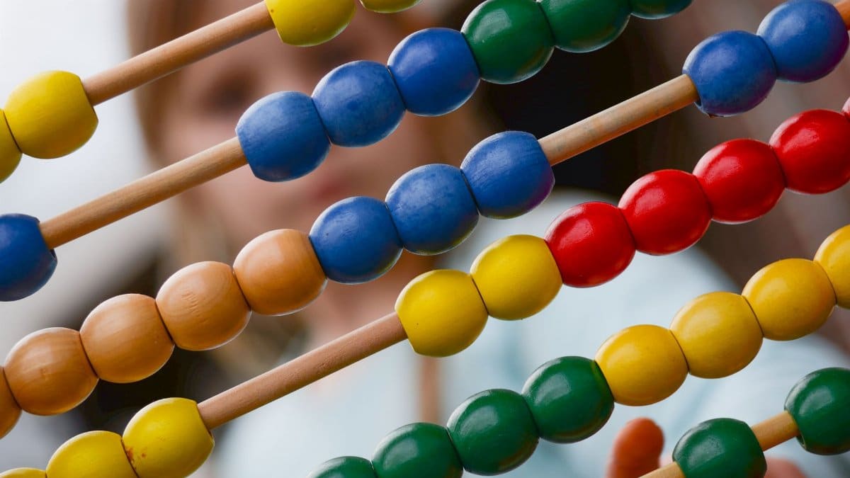 Close-up of colorful wooden abacus with a child learning math in the background, focusing on education and early childhood development.
