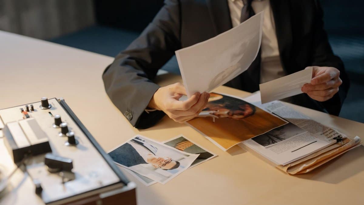 Close-up of a detective in a suit analyzing photographic evidence at a desk, suggesting investigation or inquiry.