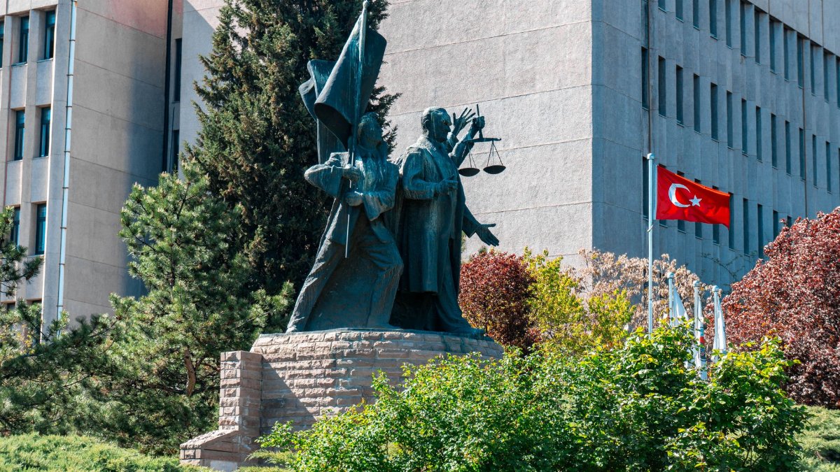Monument before a government building in Ankara, Turkey, featuring flags and greenery.