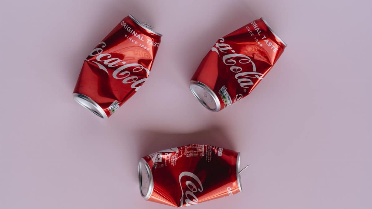 Three crumpled Coca-Cola cans arranged on a pink surface, emphasizing recycling.