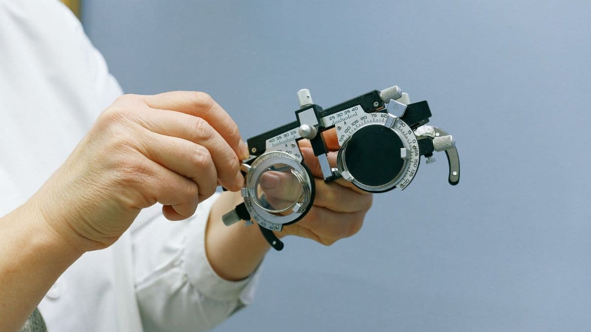 Crop unrecognizable doctor in white coat standing on blue background and showing vision test glasses with metal and plastic parts and measuring scale