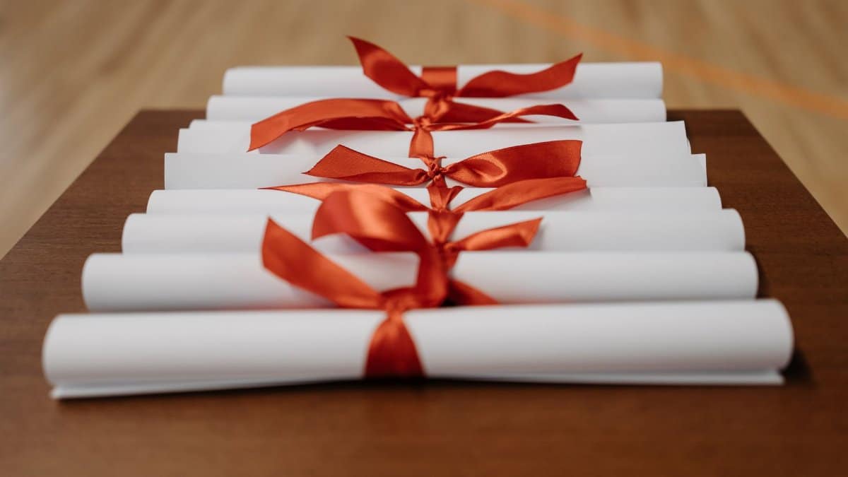 Close-up of rolled diplomas tied with red ribbons on a wooden desk, ready for presentation.