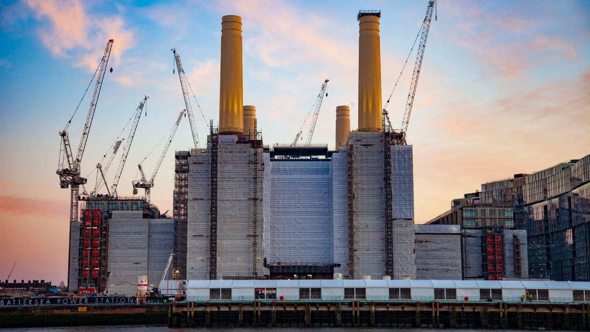 Battersea Power Station during redevelopment with cranes against a vibrant sunset sky in London, England.
