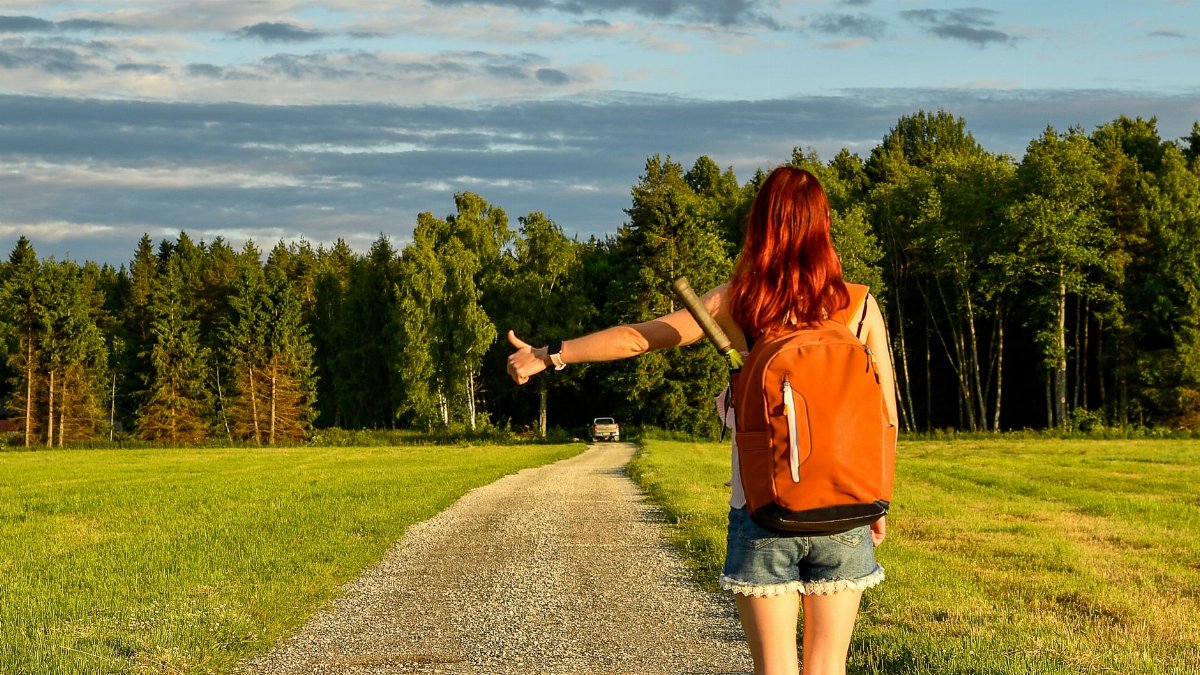 A woman with a backpack hitchhiking on a gravel road during a summer evening in Kolga, Estonia.