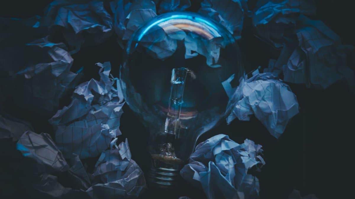 A light bulb surrounded by crumpled paper symbolizes creative ideas and innovation in a dark setting.