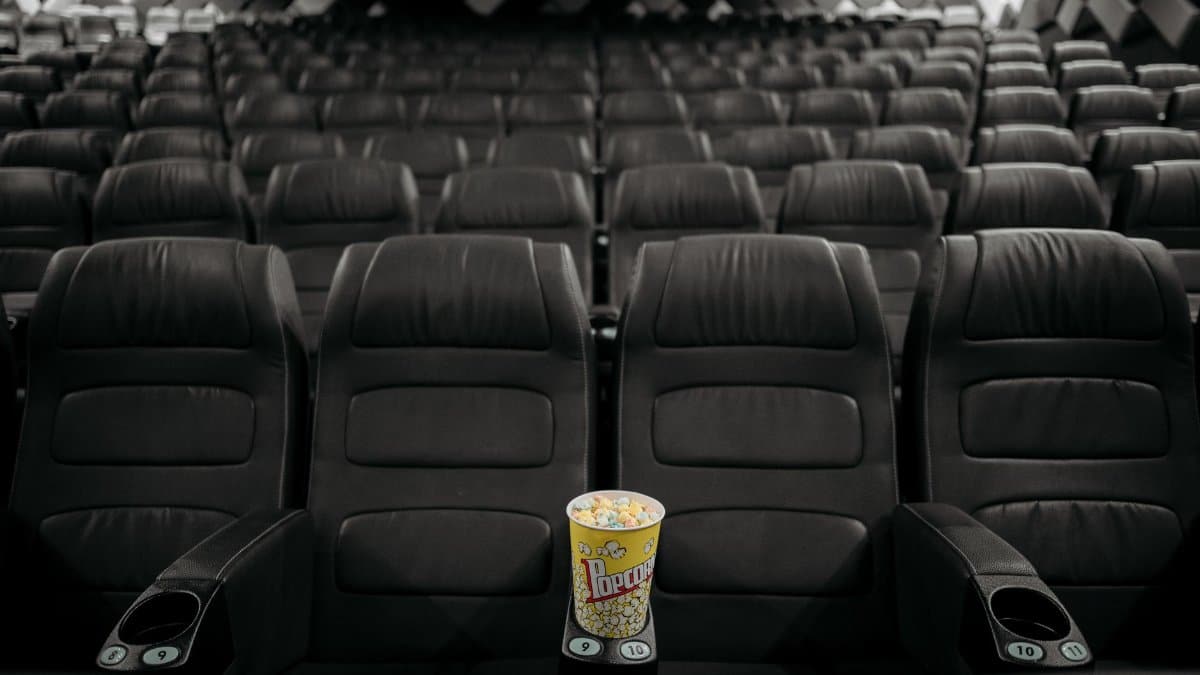 An empty cinema hall with black leather seats and a bucket of popcorn on an armrest.
