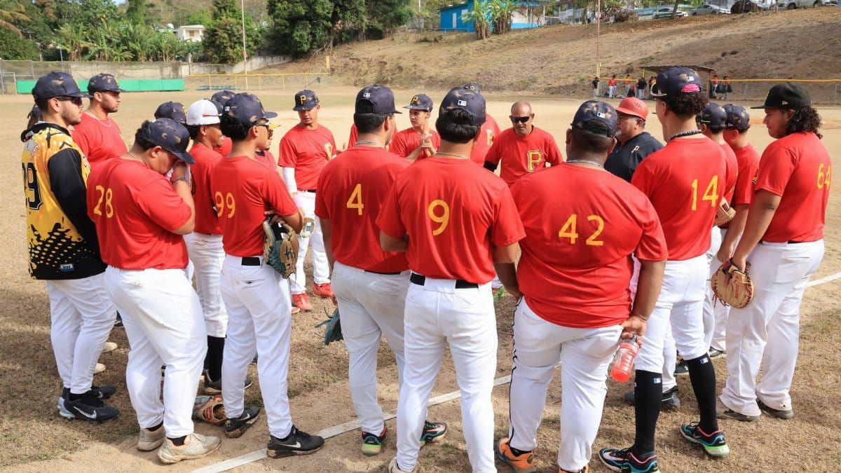 Baseball team in red jerseys gathers for a pre-game strategy session on a sunny day.