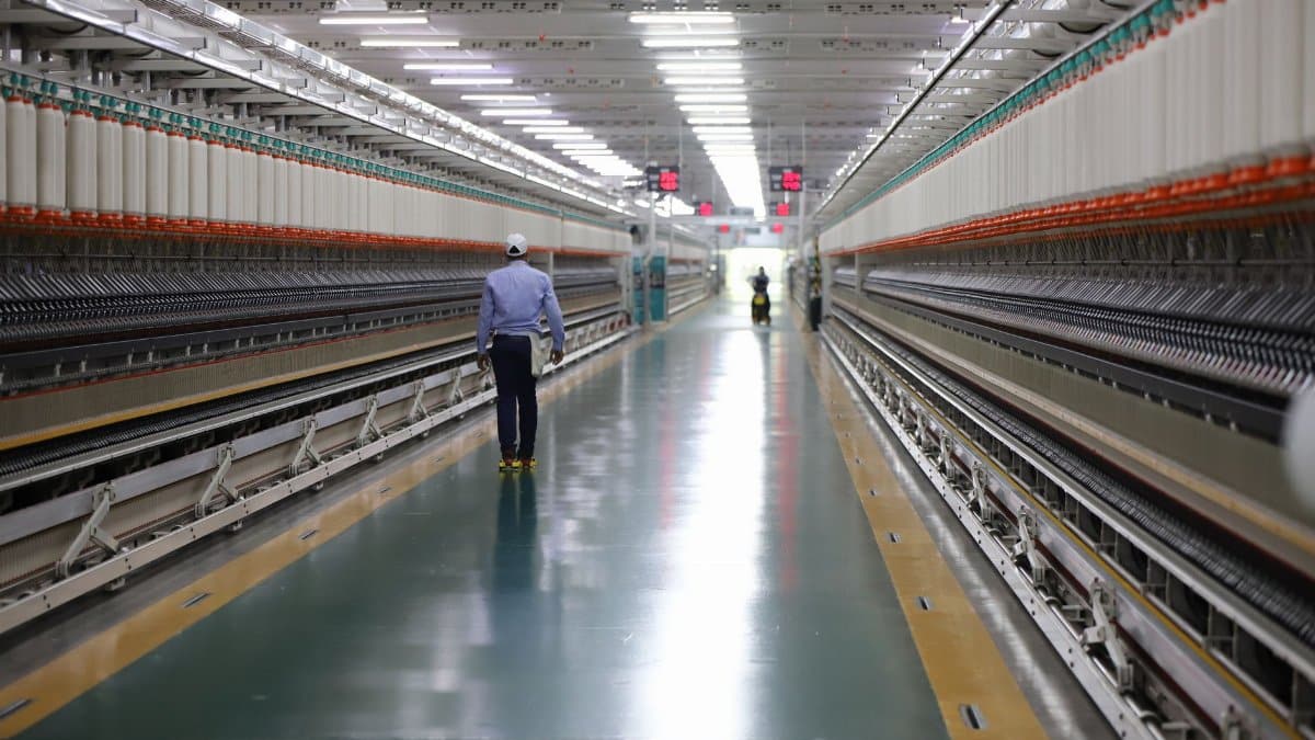 A man walks through a well-lit hallway in a modern industrial textile plant in India.