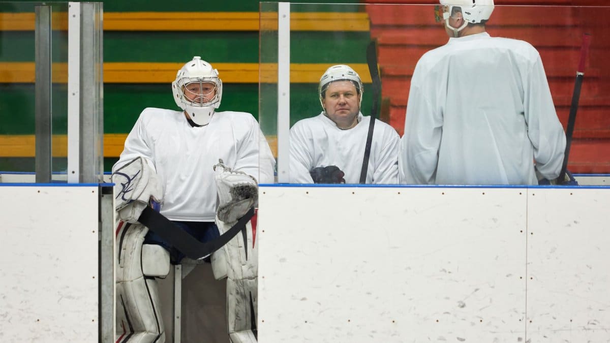 Hockey players in uniforms sitting on the bench during a game pause inside the ice rink.