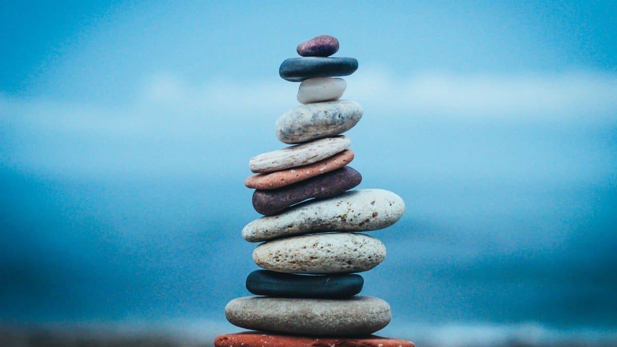 Closeup of stacked flat stones of various sizes and colors arranged on beach against blurred blue waving sea