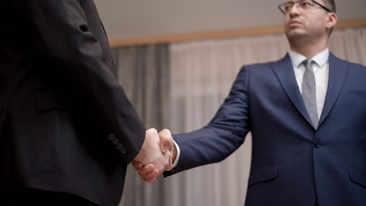 Two businessmen in formal attire shaking hands during a meeting.