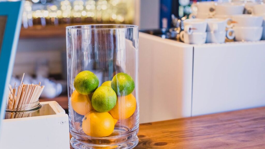 Elegant still life featuring fresh limes and oranges in a glass vase on a wooden table.