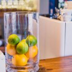 Elegant still life featuring fresh limes and oranges in a glass vase on a wooden table.