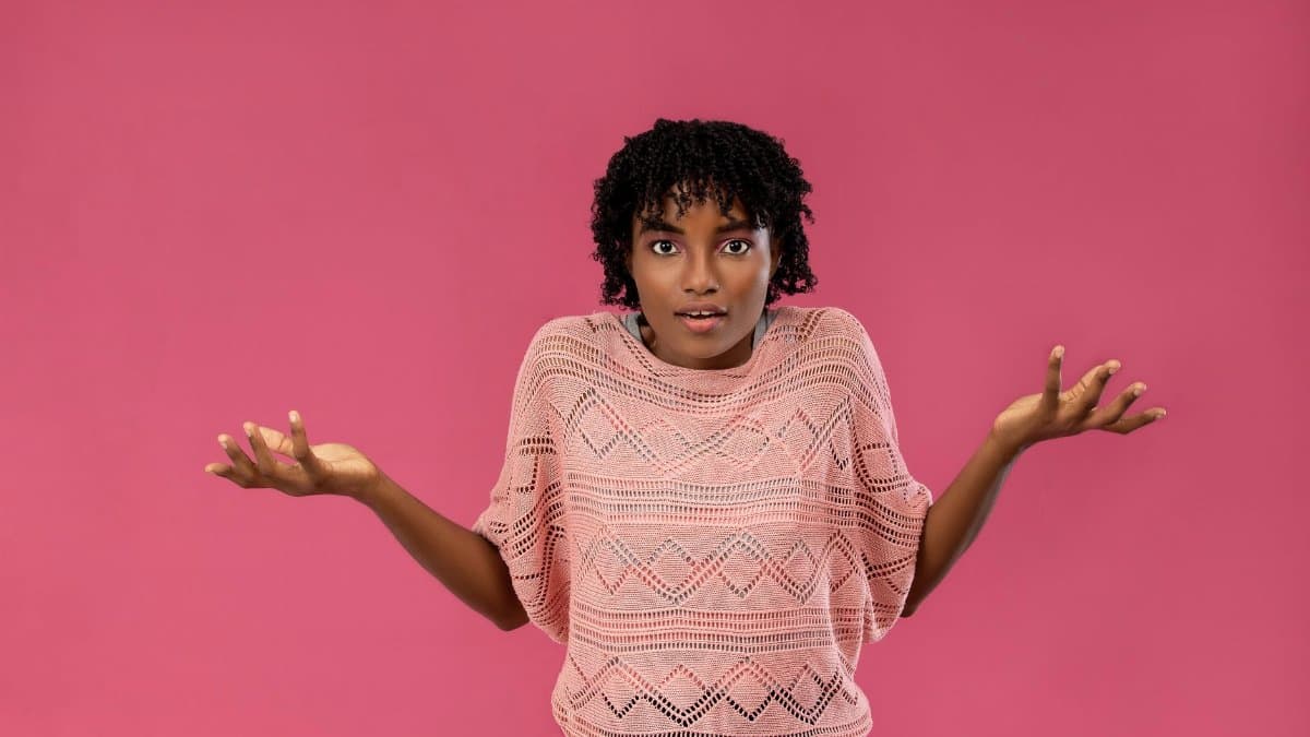 Young woman expressing confusion or uncertainty with a puzzled look on a pink background.