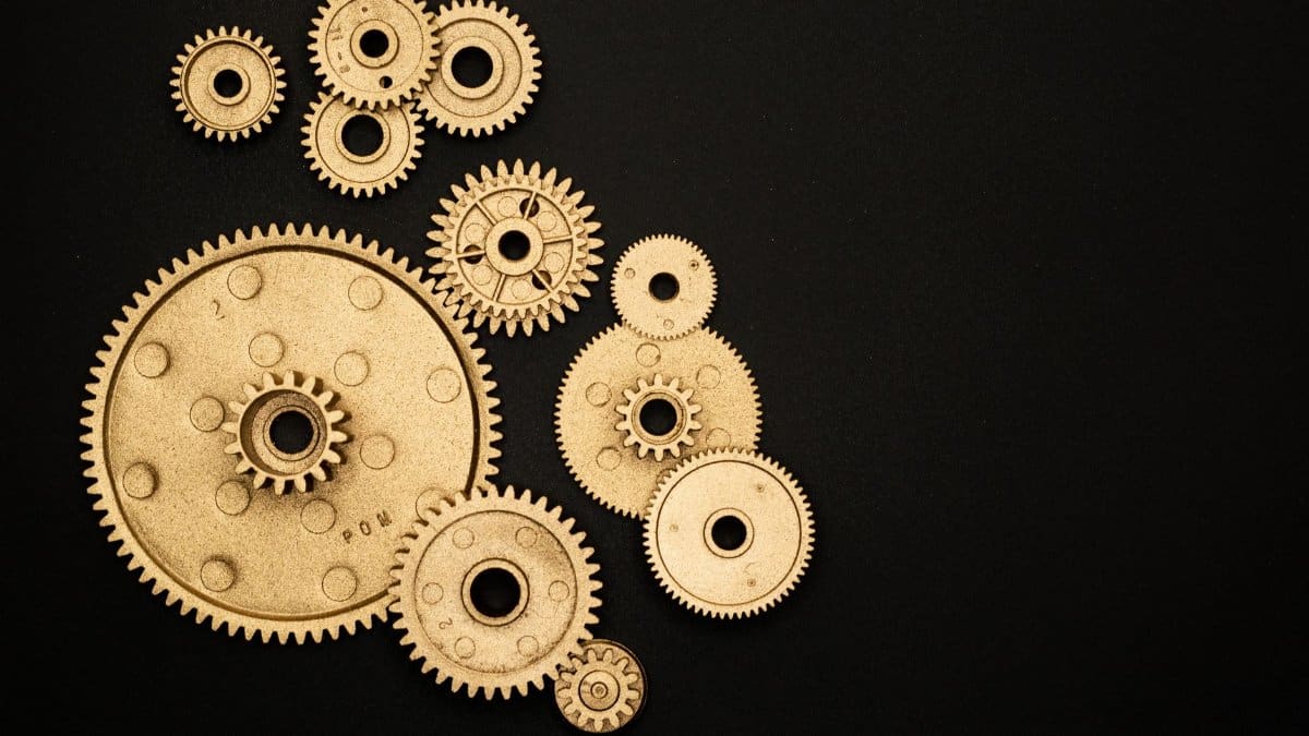 Close-up of gold gears arranged on a black backdrop, symbolizing teamwork and technology.