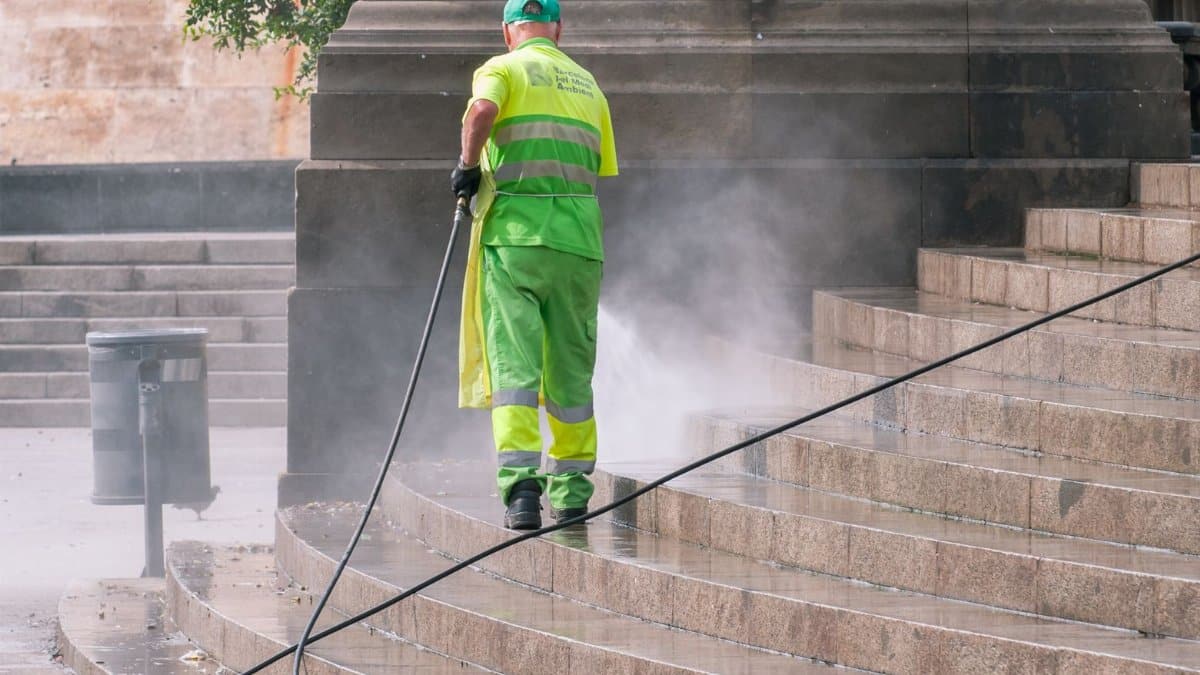 A municipal worker power washing stone steps outdoors, ensuring cleanliness and maintenance.