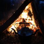 A warm campfire with a kettle, set against the tranquility of nighttime outdoors.