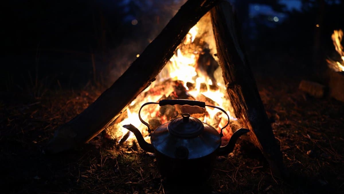 A warm campfire with a kettle, set against the tranquility of nighttime outdoors.