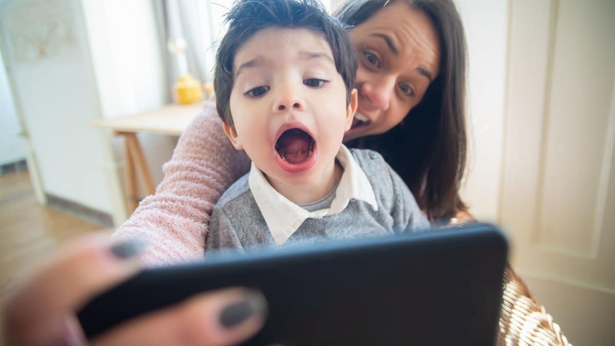 Joyful mother and son taking a selfie together indoors, capturing a fun moment.