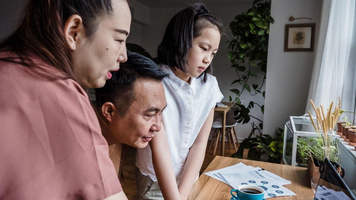 Asian family working together on a home project using a computer and notes.