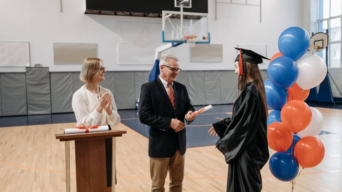 A graduate receives a diploma during an indoor ceremony in a sports hall.